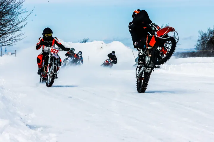 Moto et course d'auto sur glace — pilote en wheelie sur la neige